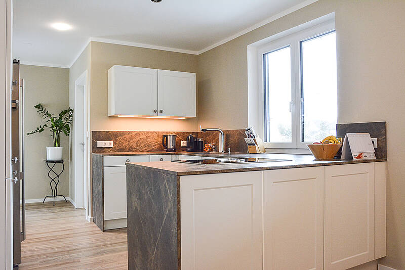 U-Küche mit Küchenzeile und Naturstein-Arbeitsplatte, das Augenmerk gilt aber den Fronten im Landhaus-Stil.