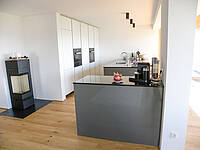 Wohnküche in weiß, grau und schwarz mit integrierten Essplatz.