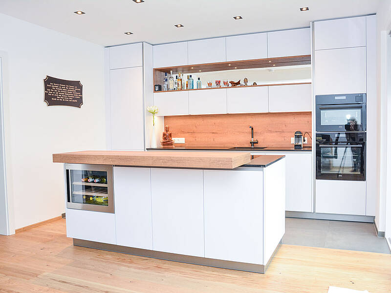 Küchenzeile in weiß und mit Holzdekor veredelt. Die Kochinsel ist mit einer Steinarbeitsplatte und dem BORA-Abluftsystem ausgestattet.