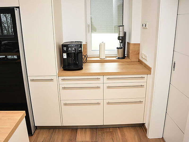 Wohnküche in Weiß und Holz mit Side-by-Side Kühlschrank, BORA-Abluftsystem und ausziehbaren Essplatz.