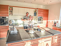 Küchen-Wandverbau mit Kochinsel in Holz-Optik und das Waschbecken integriert in Wandverbau.