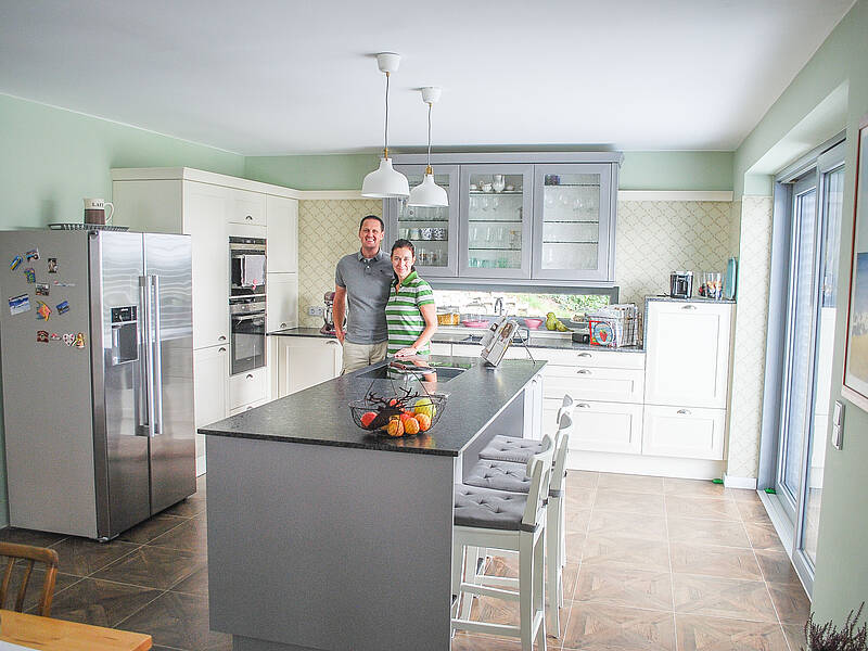 Eine Landhaus-Küche in creme/grau mit freistehenden Kühlschrank und integrierter Bar- Essplatz-Lösung.