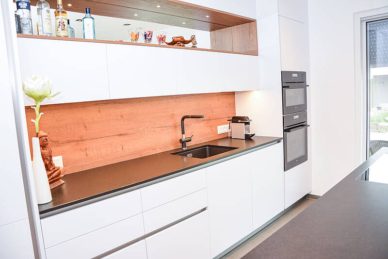 Küchenzeile in weiß und mit Holzdekor veredelt. Die Kochinsel ist mit einer Steinarbeitsplatte und dem BORA-Abluftsystem ausgestattet.