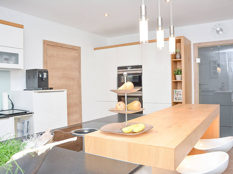 U-Küche in weiß und Holz-Optik mit integrierter Barlösung und einem schönen Essplatz.