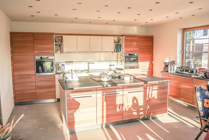 Küchen-Wandverbau mit Kochinsel in Holz-Optik und das Waschbecken integriert in Wandverbau.