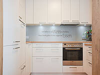 Vollintegrierte Küche in U-Form und Naturholz-Optik mit weißen Fronten.