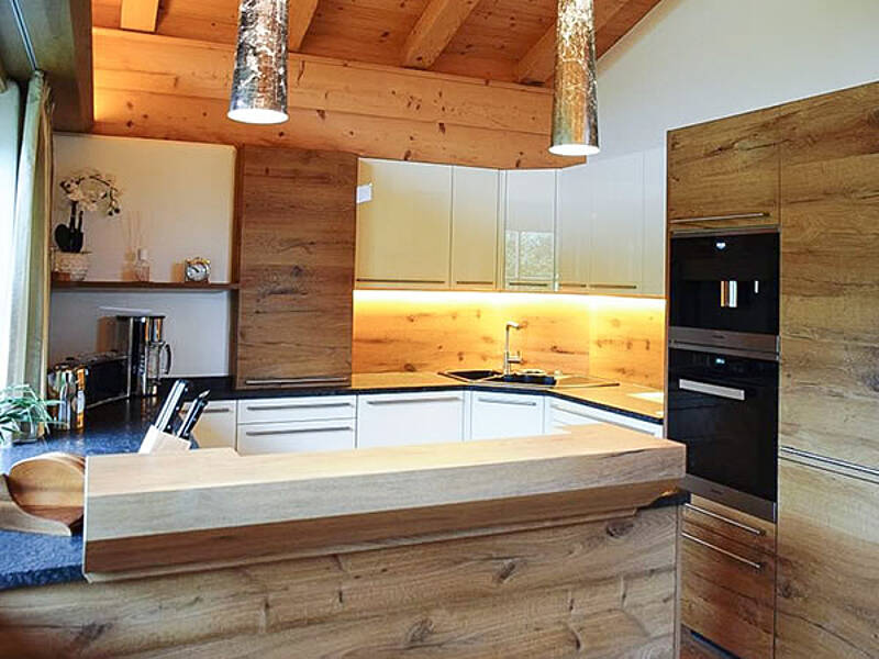 Küche in Holz-Optik mit der Spüle im Eck und integrierter Stehbar.

