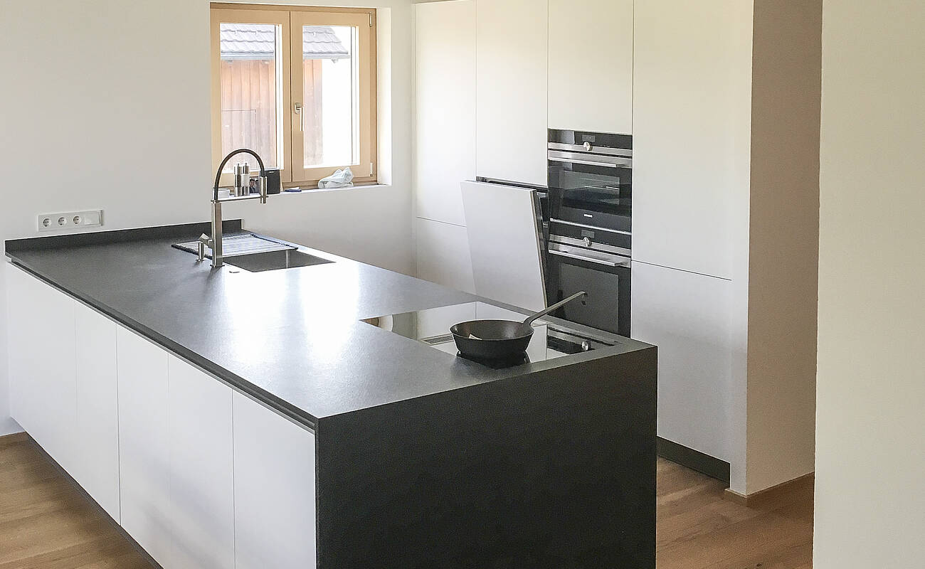 Küchenzeile in weiß mit schwarzer Kochinsel und BORA-Abluftsystem.