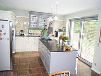 Eine Landhaus-Küche in creme/grau mit freistehenden Kühlschrank und integrierter Bar- Essplatz-Lösung.