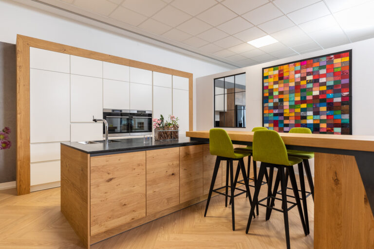 olina Küche mit weißen Hochschränken und Insel in Eiche natur mit schwarer Natursteinarbeitsplatte. Bartheke als Aufsatz mit grünen Hockern